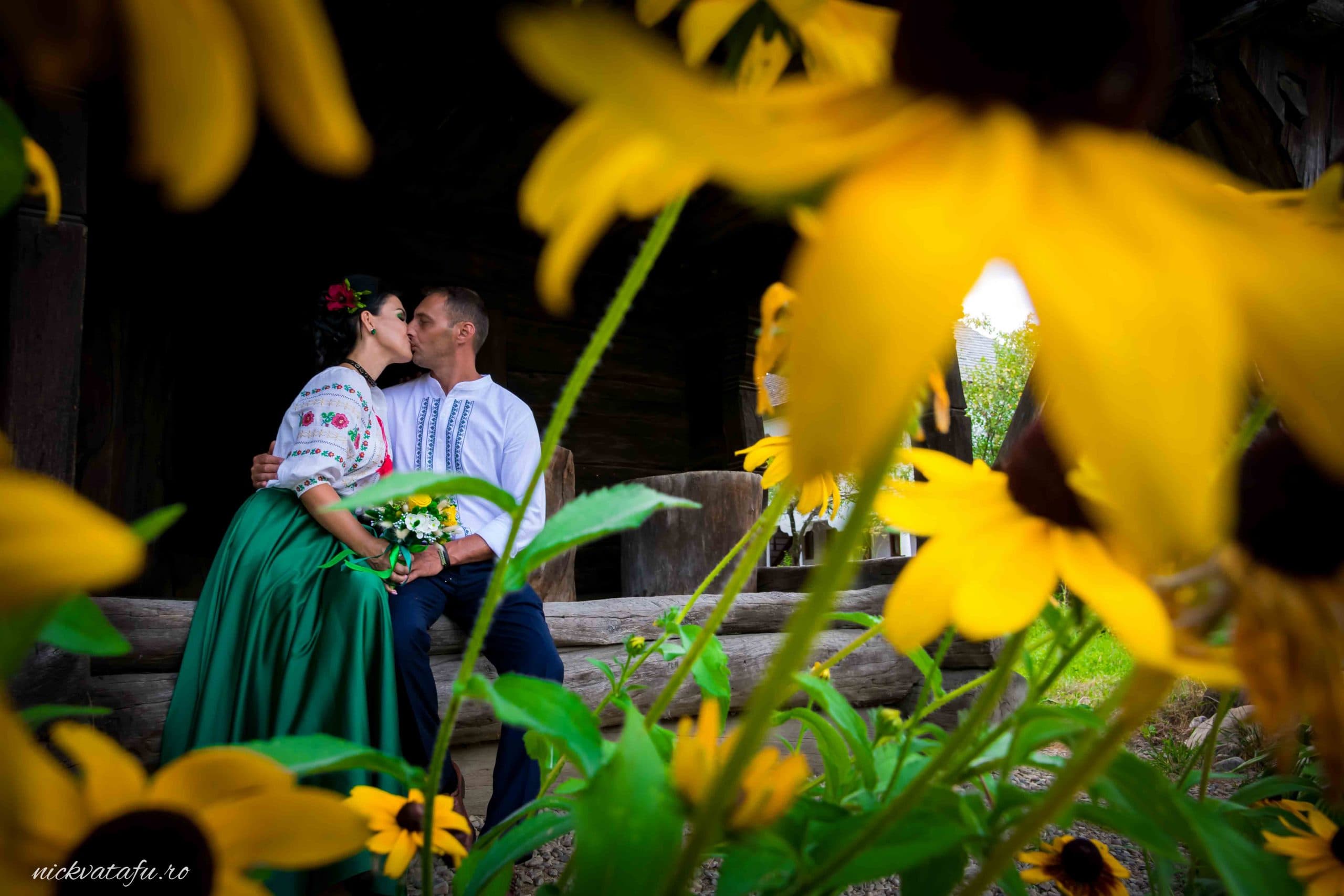 Mire și mireasă sărutându-se, înconjurați de flori galbene, fotografie de nuntă plină de emoție și romantism.
