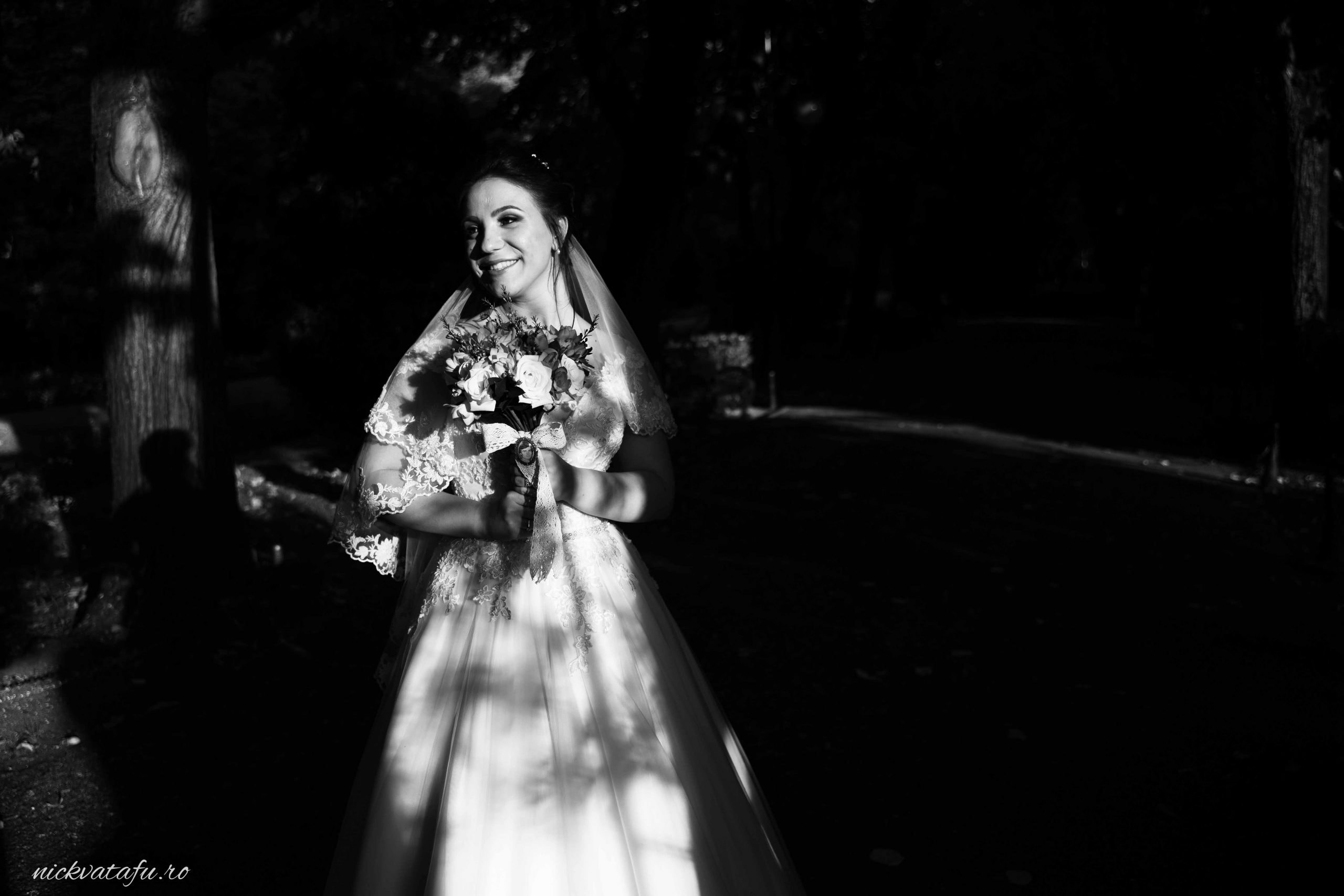 Mireasă zâmbitoare cu buchet de flori, surprinsă în lumini și umbre, fotografie de nuntă elegantă.