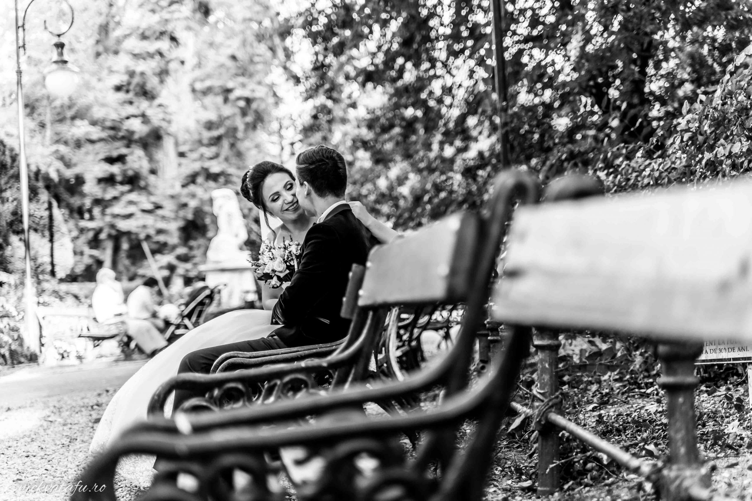 Mire și mireasă într-o discuție intimă pe o bancă, fotografie de nuntă plină de emoție în natură.