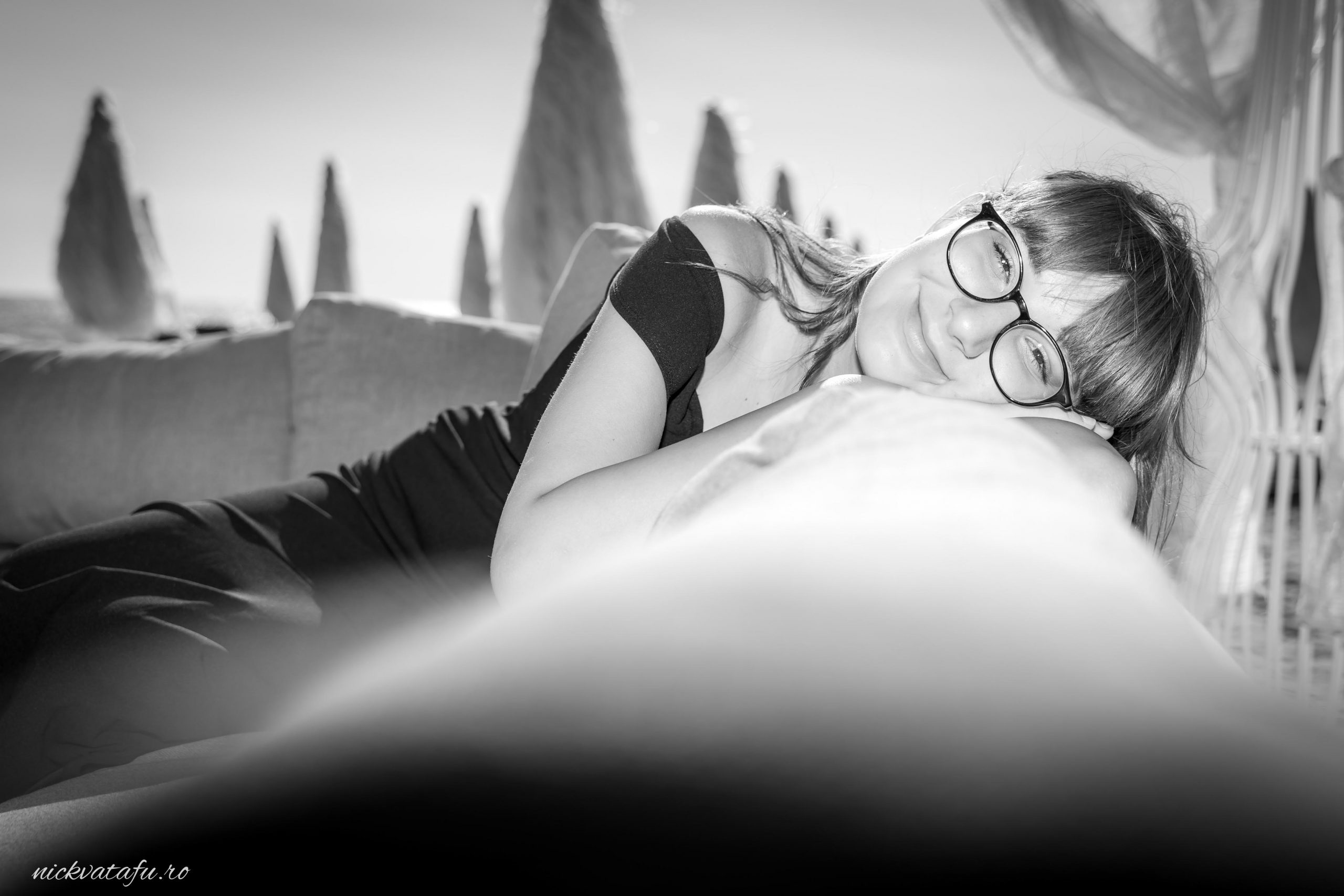 Fată zâmbitoare, relaxată, stând pe o canapea, fotografie artistică în alb și negru, evocând emoție și intimitate.