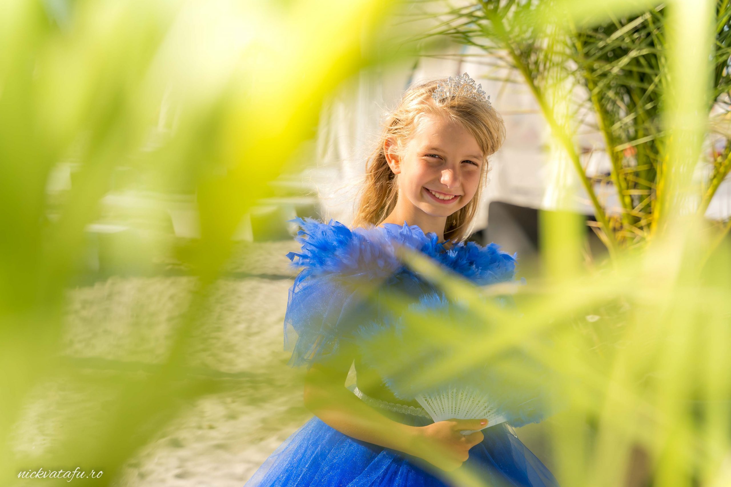 Fetiță zâmbitoare în rochie albastră, surprinsă în decorul unei petreceri, plină de emoție și bucurie.