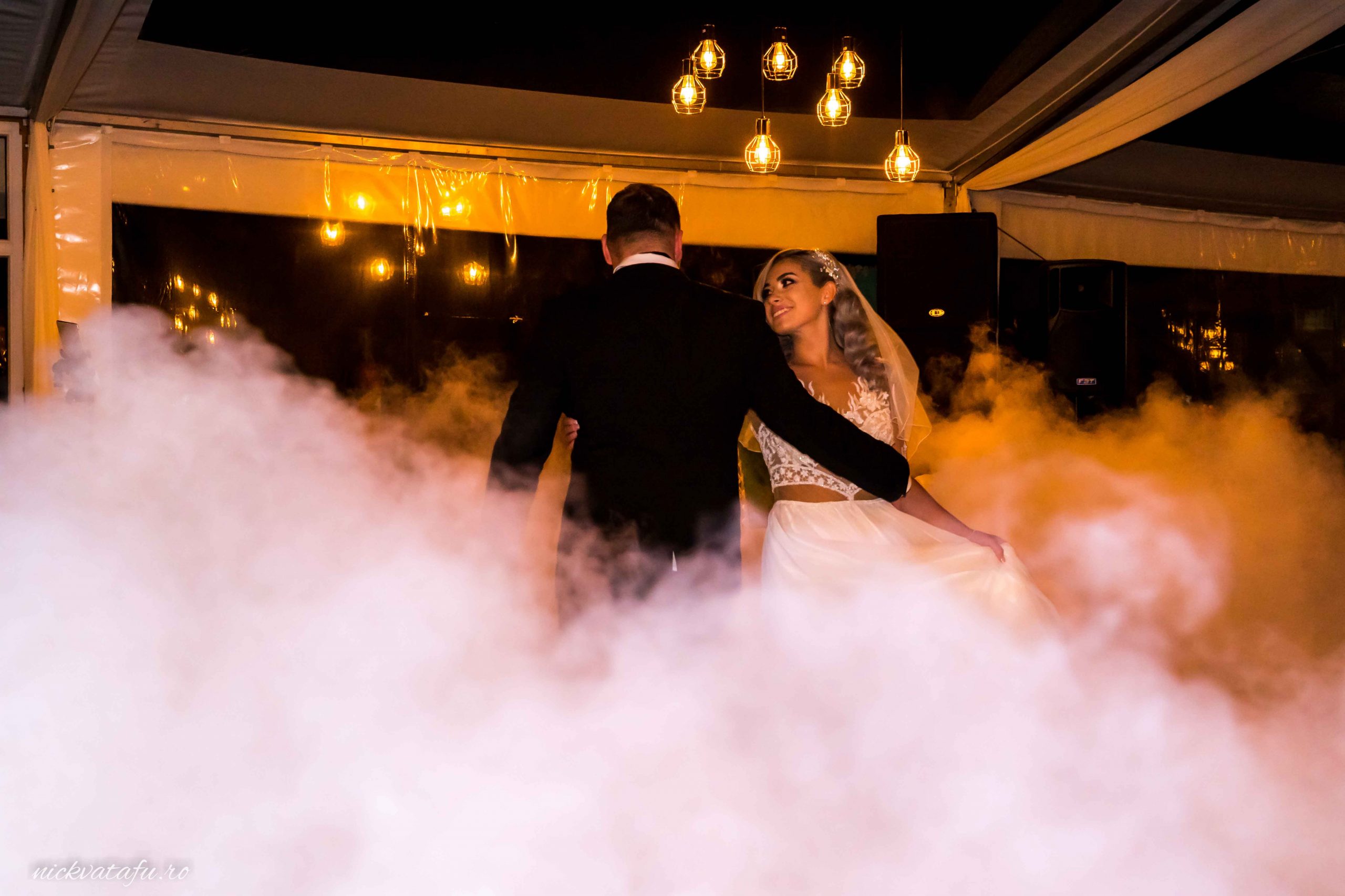 Mire și mireasă dansând într-o atmosferă romantică, învăluiți de ceață, fotografie de nuntă elegantă.