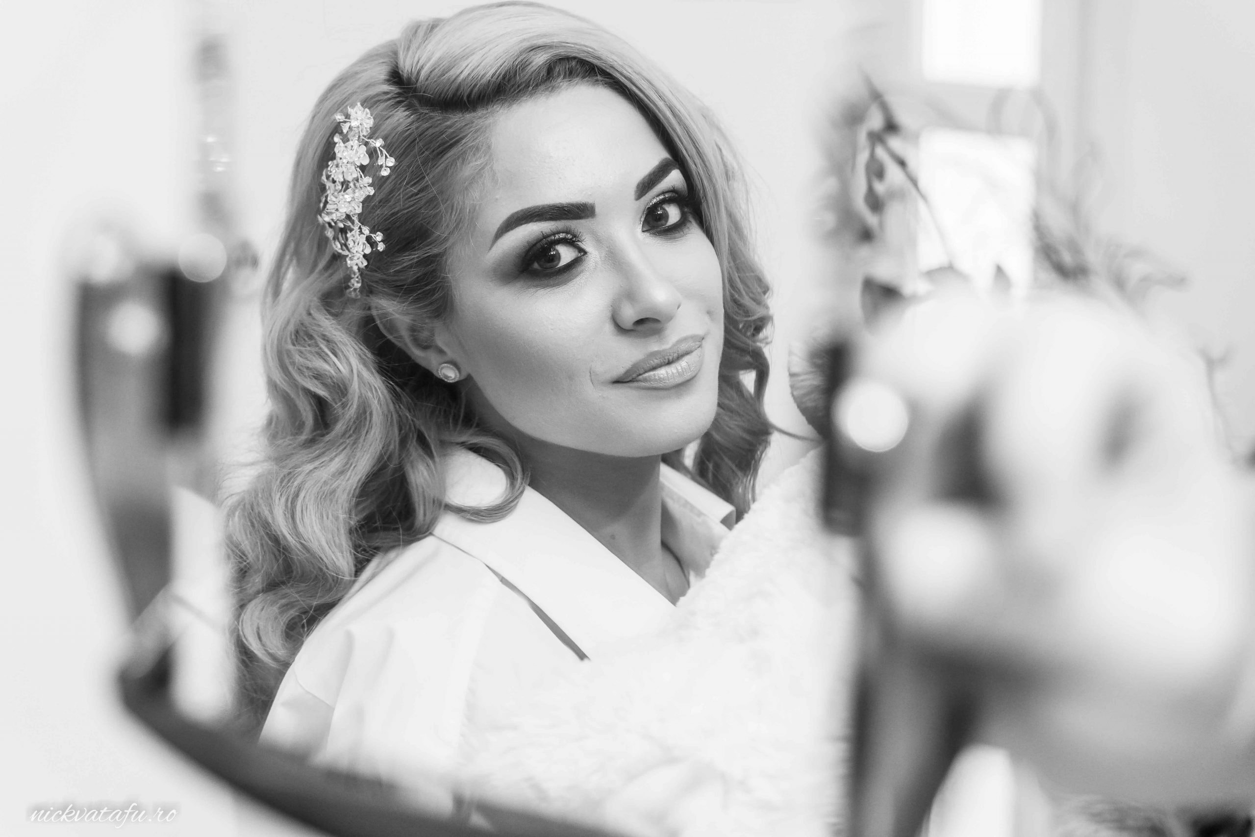 Mireasă zâmbitoare, pregătindu-se pentru nuntă, reflectată elegant în oglindă, capturând emoția momentului.