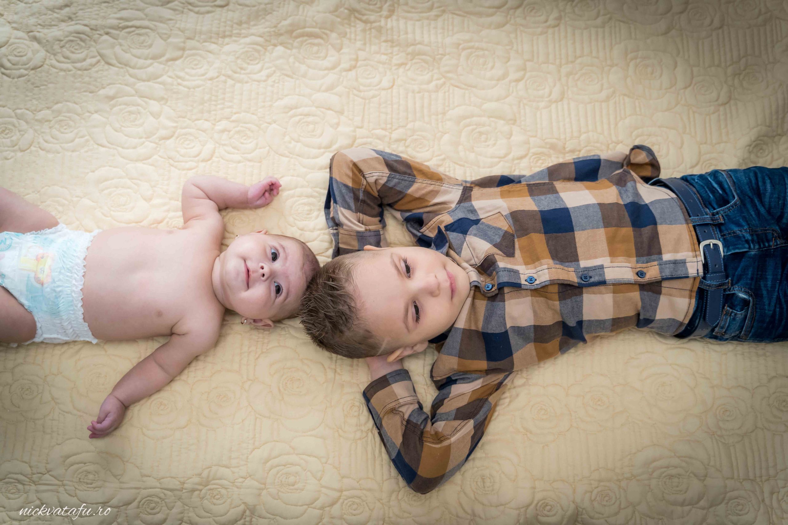 Băiat și bebeluș zâmbind pe o pătură, captura plină de emoție și inocență, perfectă pentru un botez.