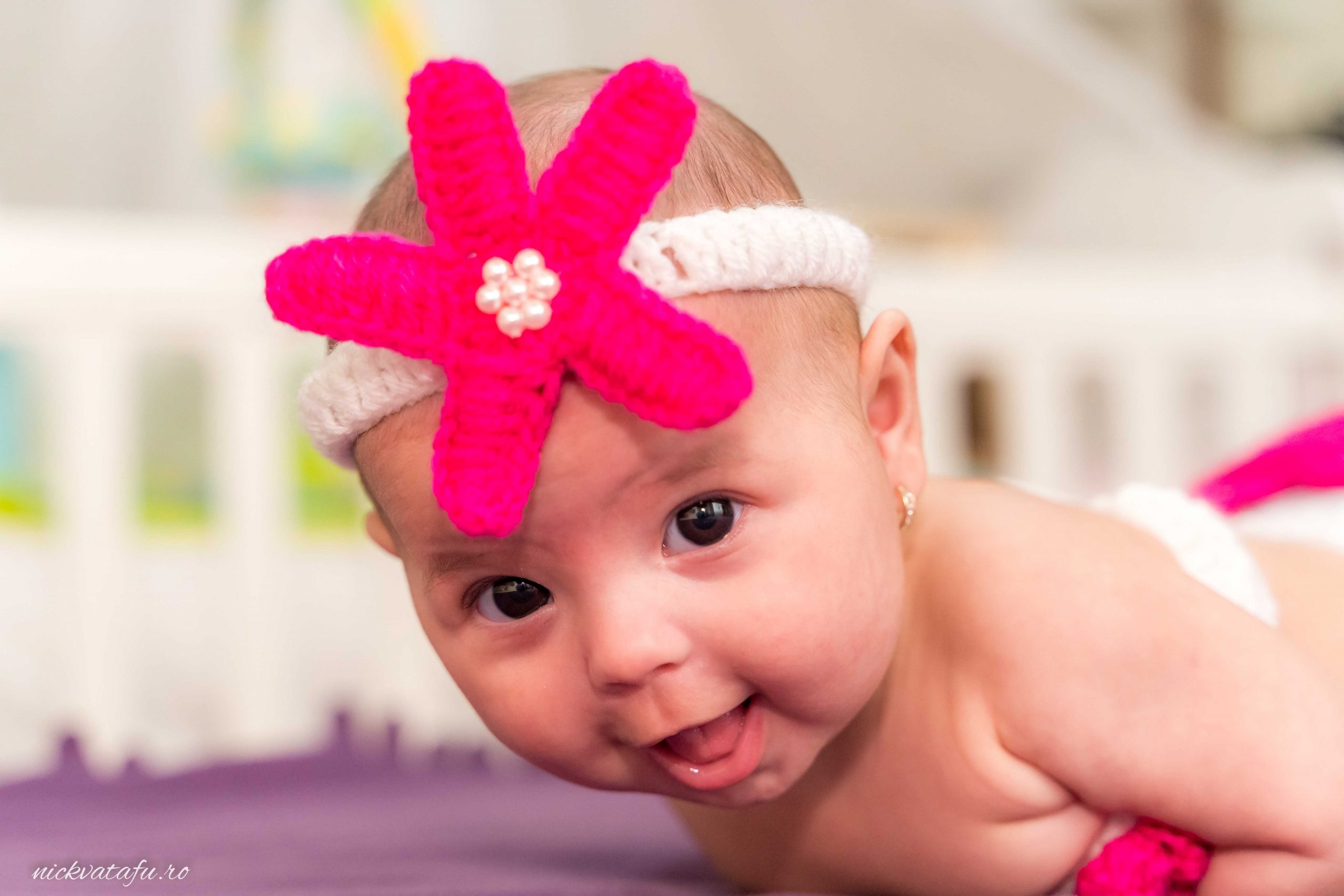 Bebeluș zâmbitor cu o bentiță roz decorată, pe un fundal luminos, fotografie de botez plină de emoție.