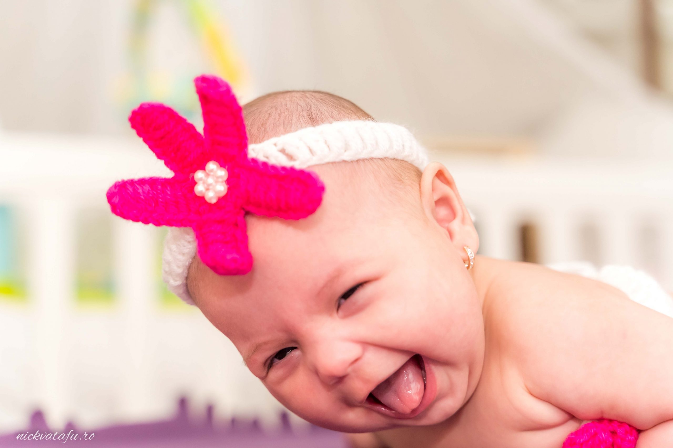 Bebeluș zâmbitor cu o bentiță roz, capturând bucuria unui botez în Pitești, fotografie plină de emoție.