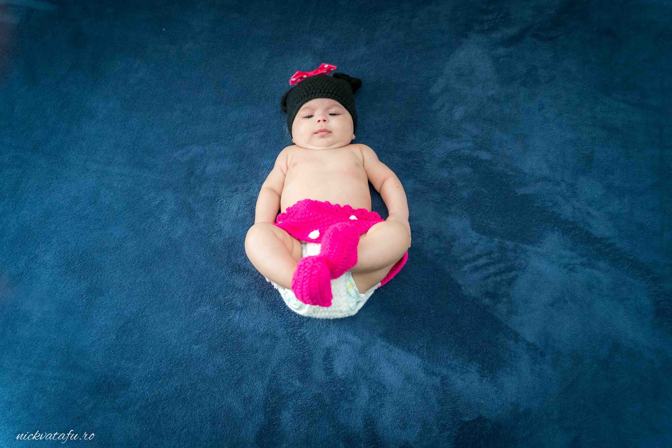 Bebeluș adorabil îmbrăcat în roz, relaxat pe o pătură albastră, fotografie emoționantă de botez.