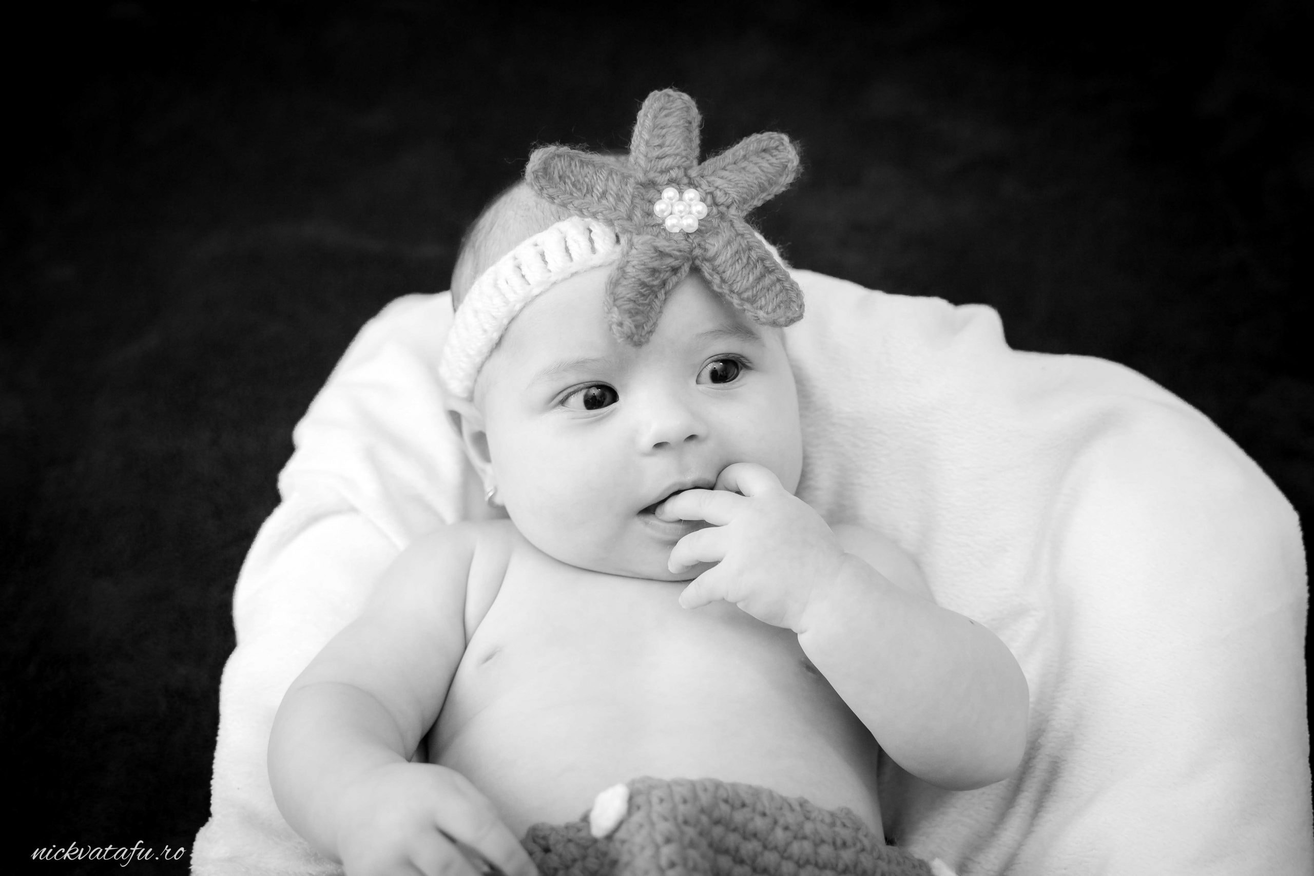 Bebeluș zâmbitor cu o bentiță decorată, capturat într-o fotografie de botez, emanând emoție și inocență.