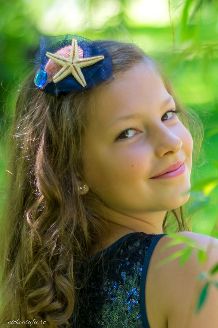 Fetiță zâmbitoare cu o pălărie decorată, înconjurată de natură, capturând emoția unui moment special.