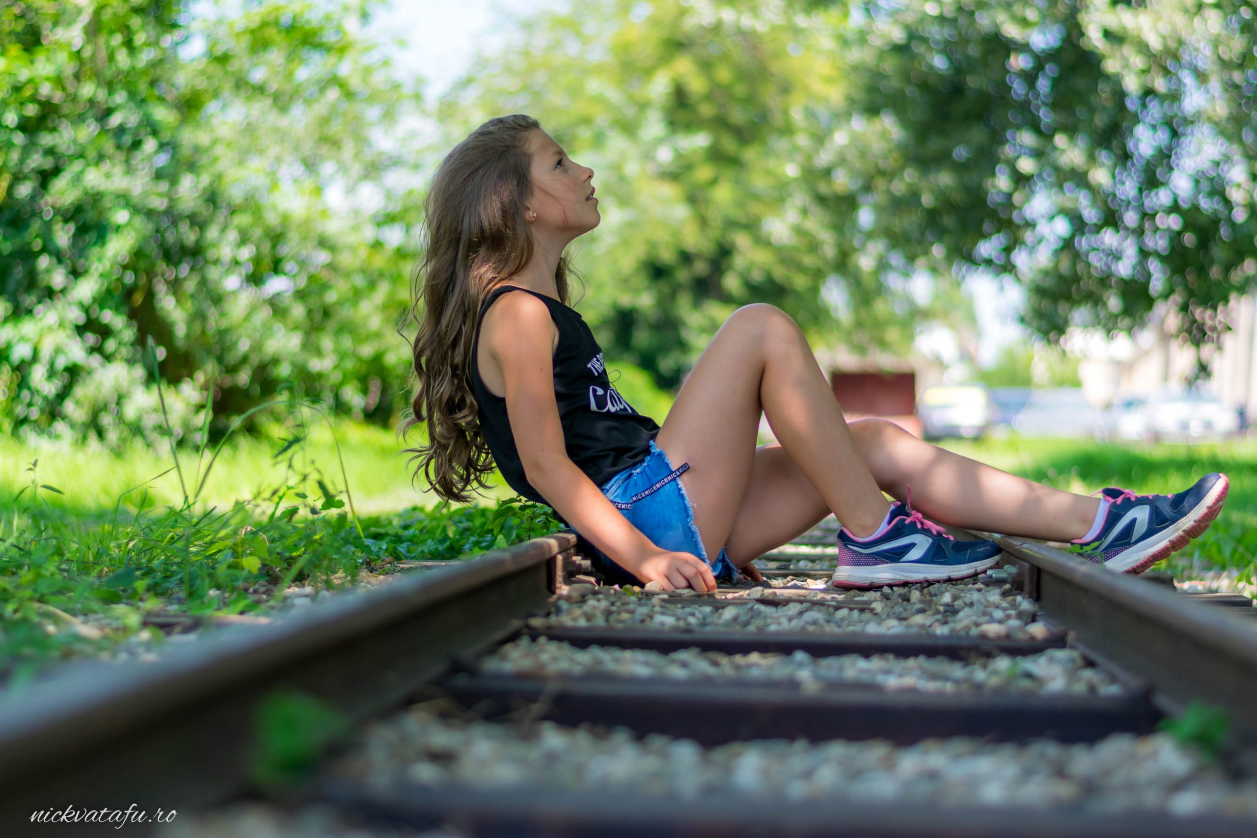 Fată relaxată pe șinele de tren, admirând natura, fotografie artistică plină de emoție și liniște.