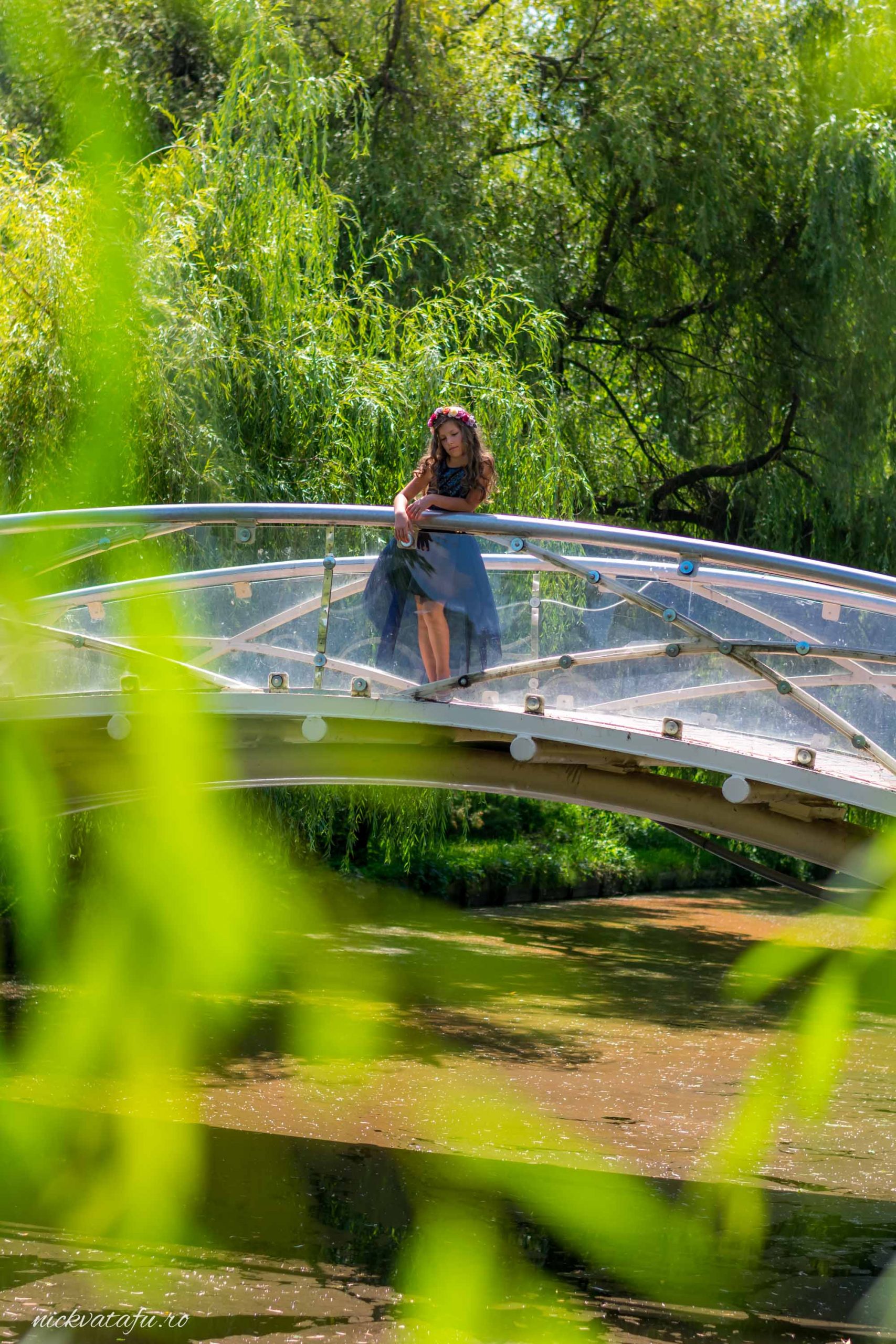 Femeie elegantă pe un pod transparent, înconjurată de natură, evocând emoții de serenitate și frumusețe în fotografie de nuntă.