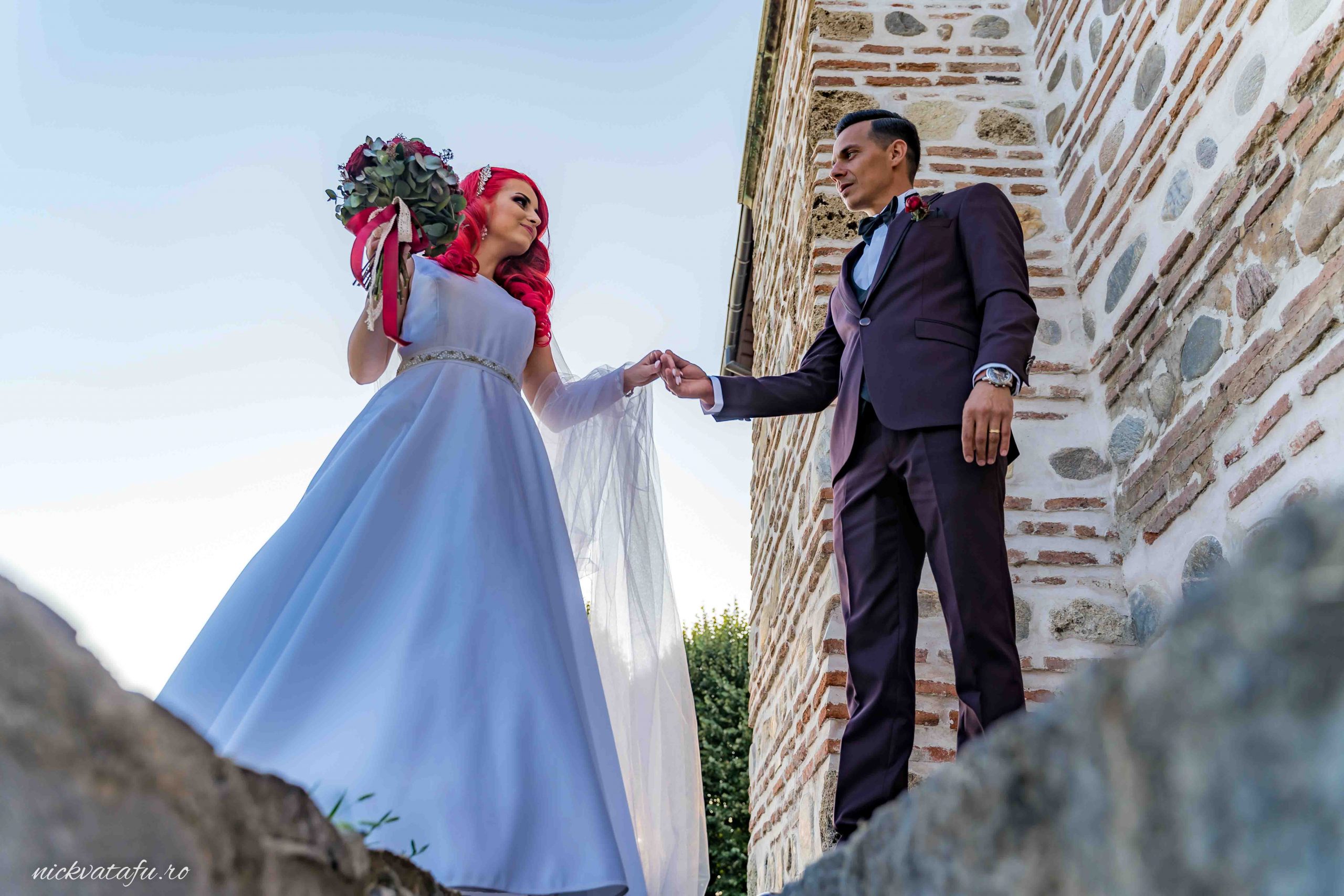 Mireasă cu rochie albă și buchet de flori, alături de mire în costum, într-o atmosferă romantică.