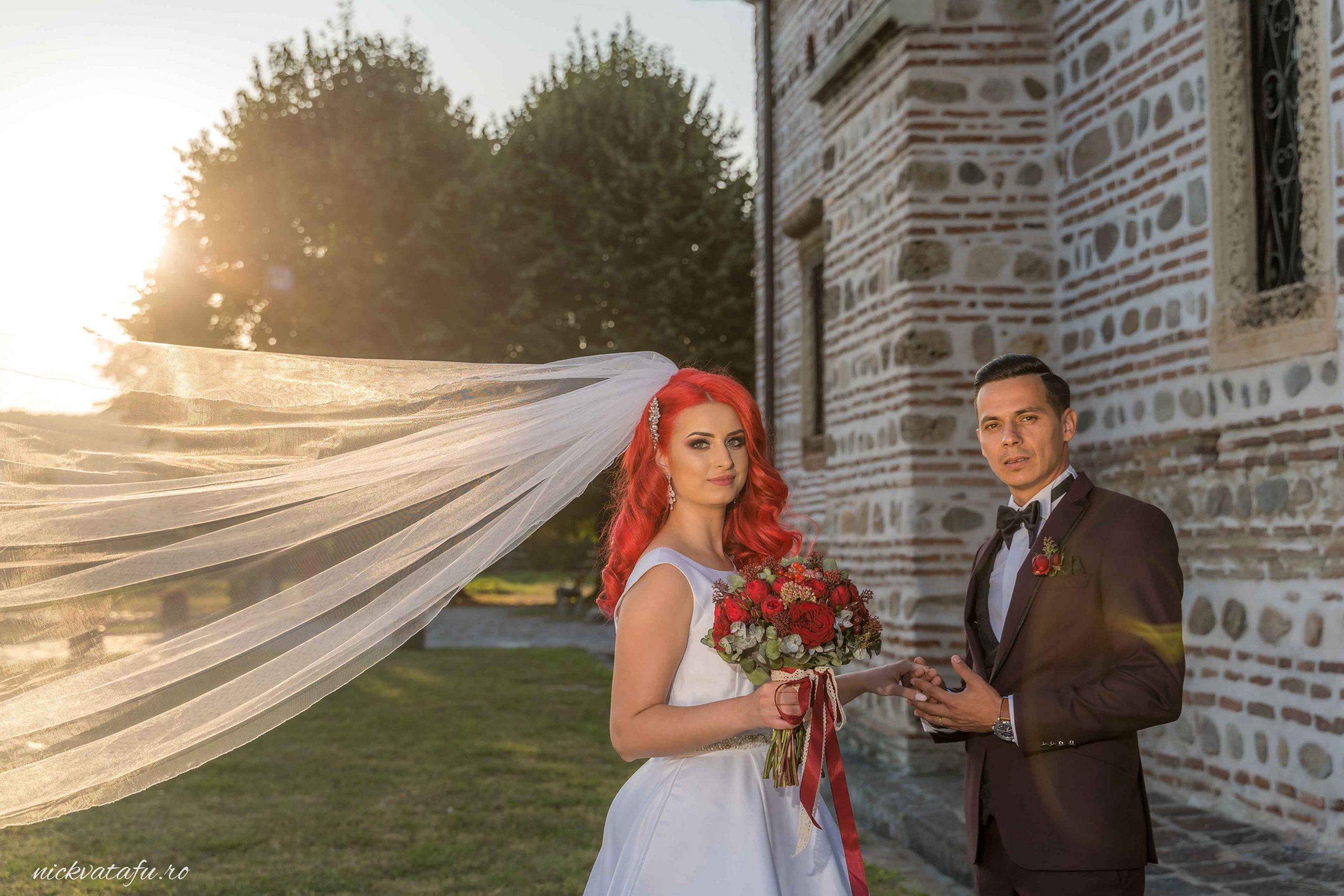 Mire și mireasă surprinși în lumina apusului, cu voalul fluturând, fotografie de nuntă elegantă.