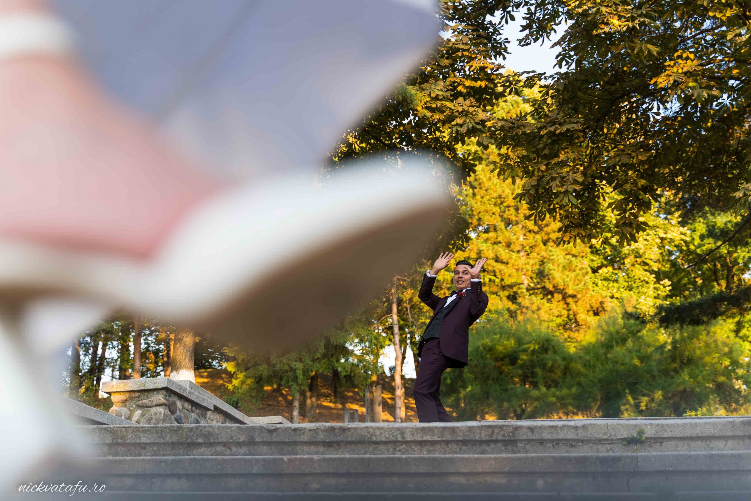 Mire și mireasă se pregătesc să danseze, plini de emoție, într-un peisaj natural deosebit.