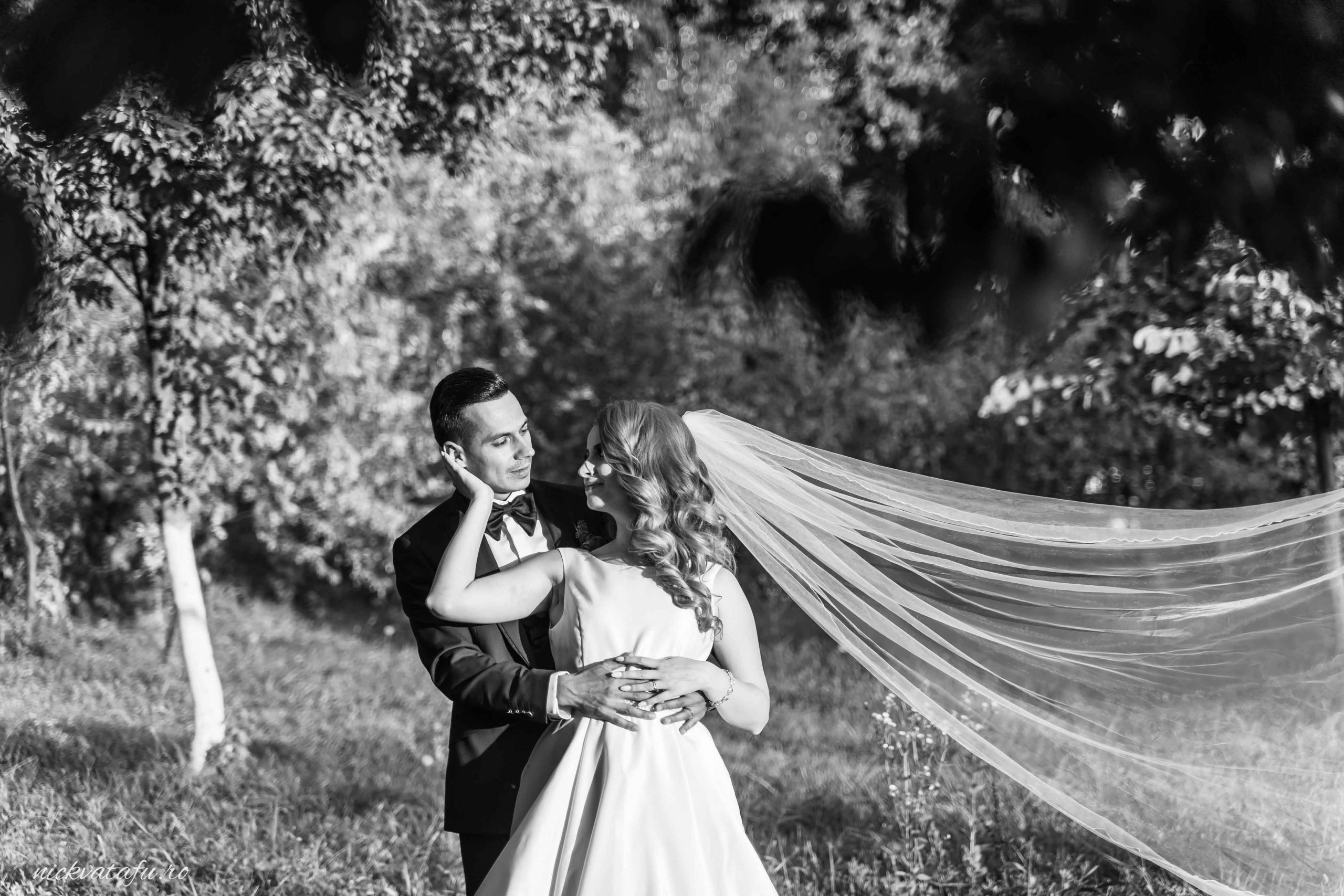 Mire și mireasă într-un moment romantic, cu voalul fluturând în vânt, fotografie elegantă de nuntă în natură.