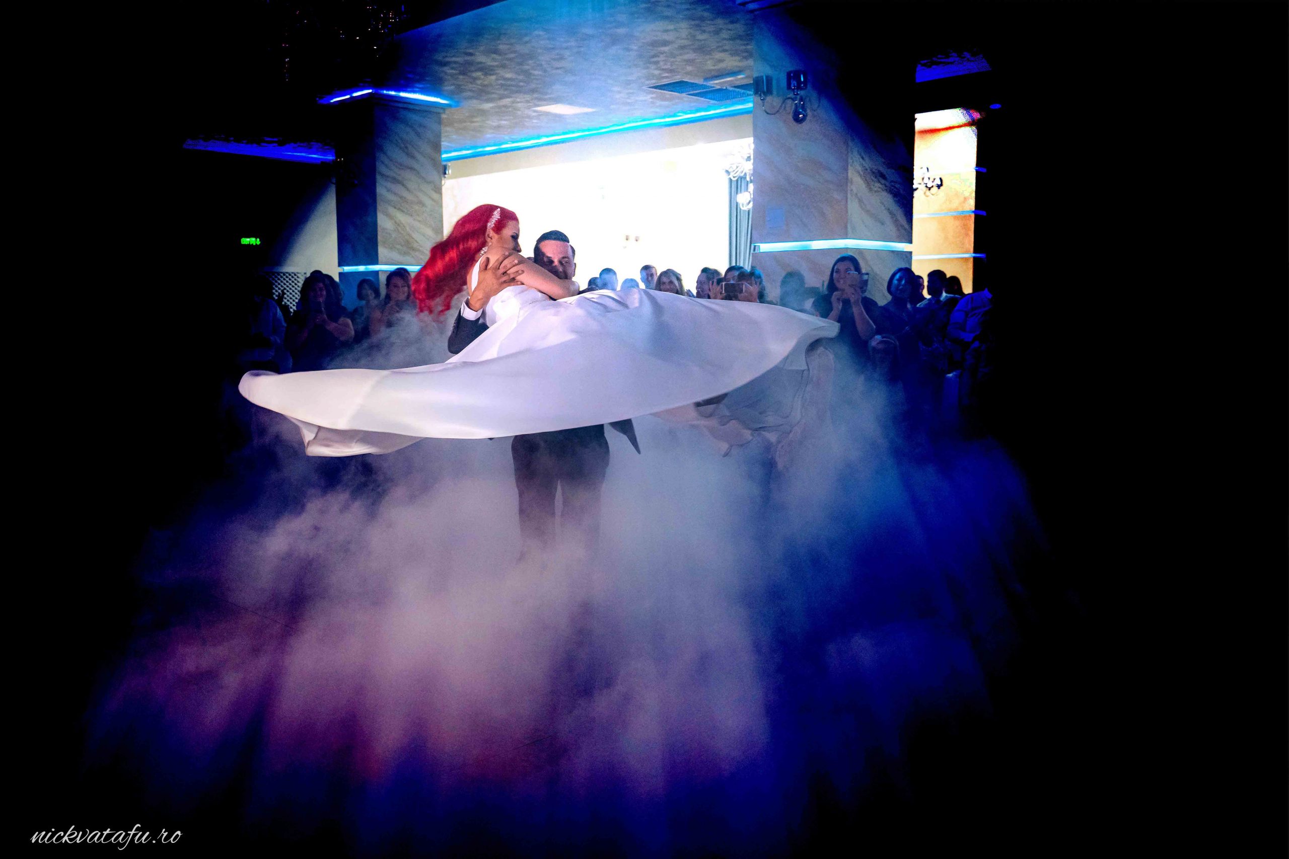 Dansul mirilor într-o atmosferă magică, cu lumini și fum, fotografie de nuntă plină de emoție.