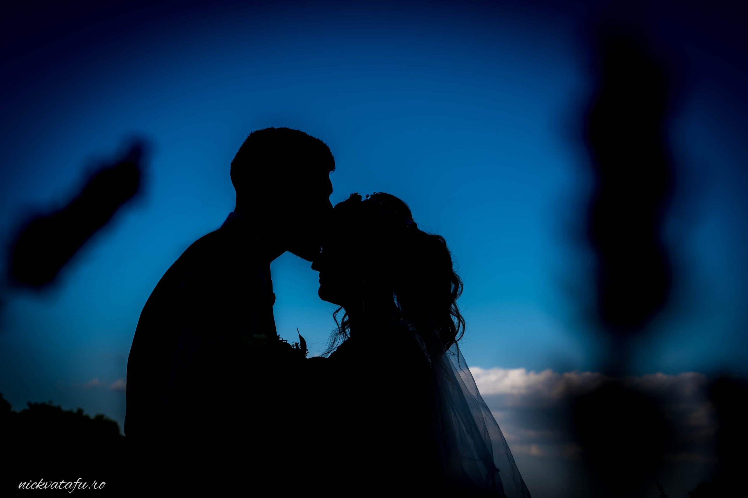 Mire și mireasă în umbra unei îmbrățișări pline de emoție, sub cerul albastru, fotografie de nuntă romantică.