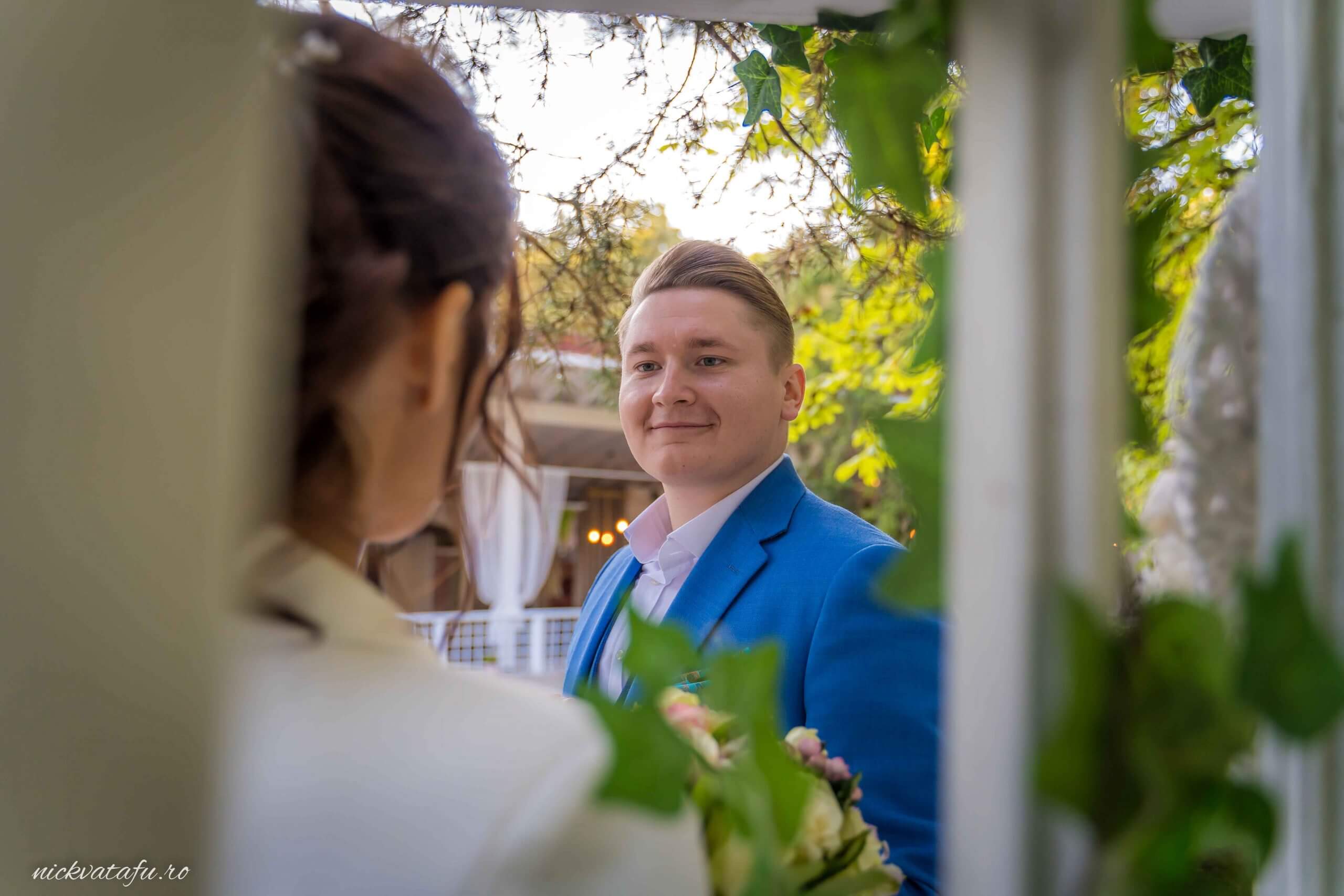 Mire și mireasă zâmbind unul către altul, înconjurați de natură, fotografie nuntă plină de emoție.