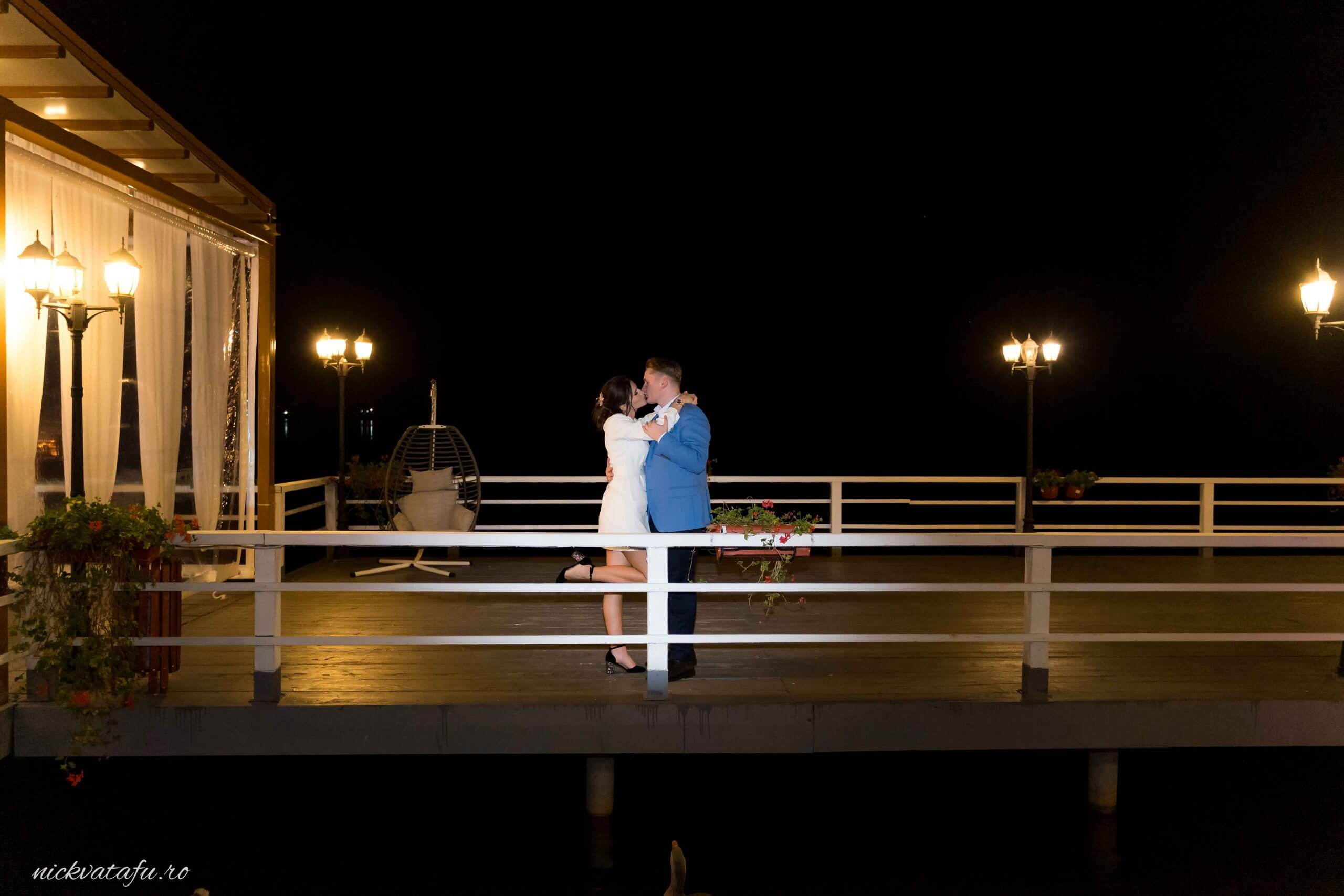 Mire și mireasă se îmbrățișează pasional pe un ponton luminat, fotografie de nuntă cu emoție nocturnă.