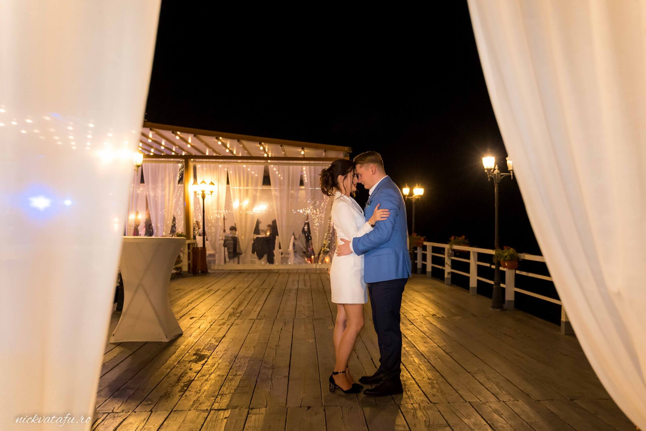 Mire și mireasă dansând romantic pe un ponton iluminat, fotografie de nuntă plină de emoție și eleganță.