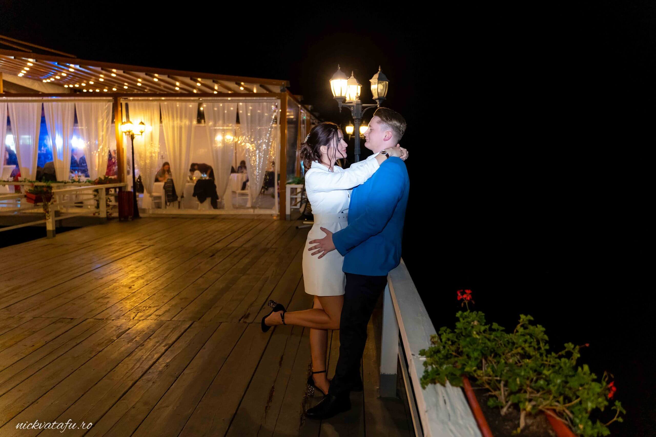 Îmbrățișare romantică pe un promenadă iluminată, fotografie de nuntă ce reflectă emoția și intimitatea cuplului.