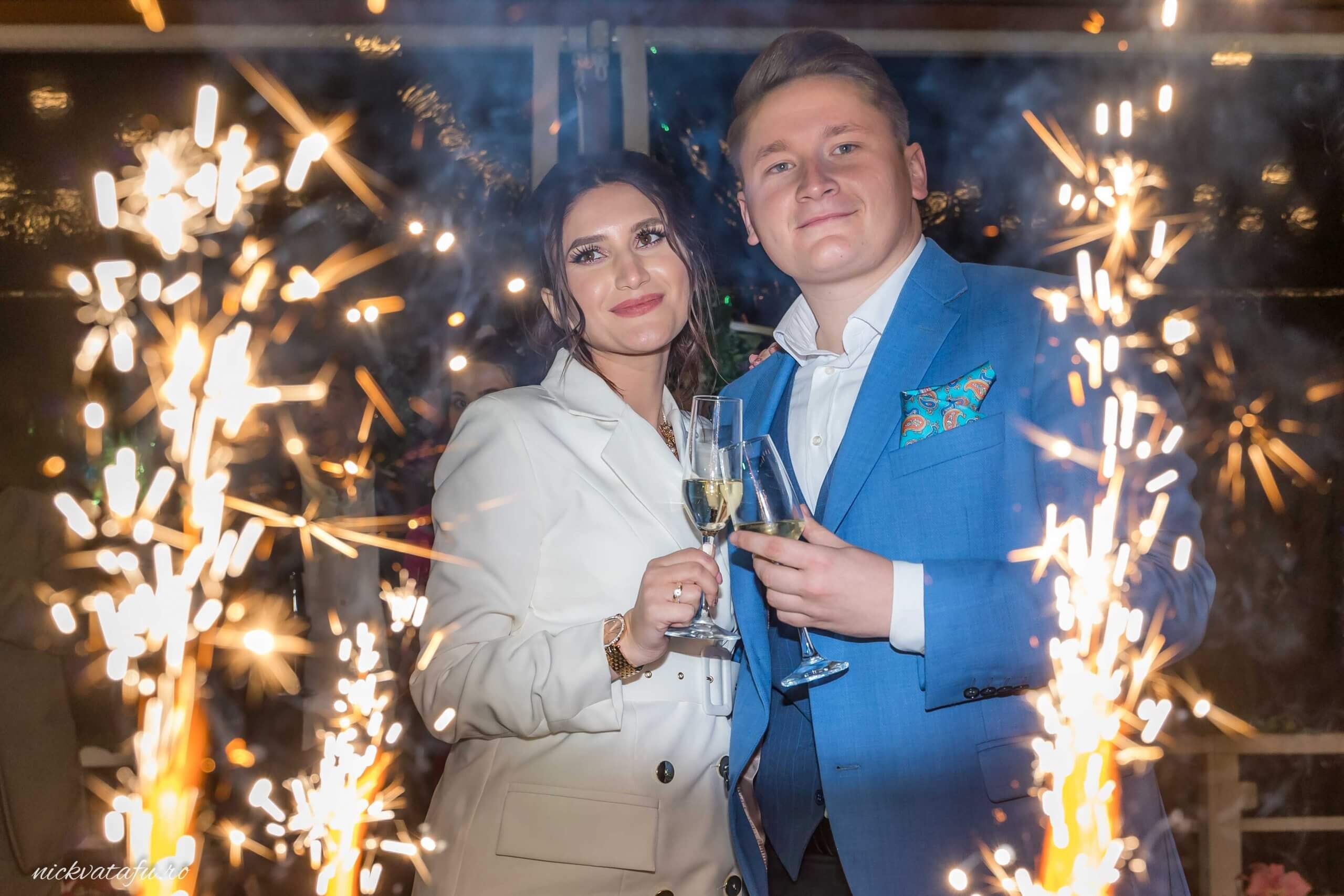 Cuplu fericit sărbătorind cu șampanie, înconjurați de artificii, fotografie de nuntă plină de emoție.