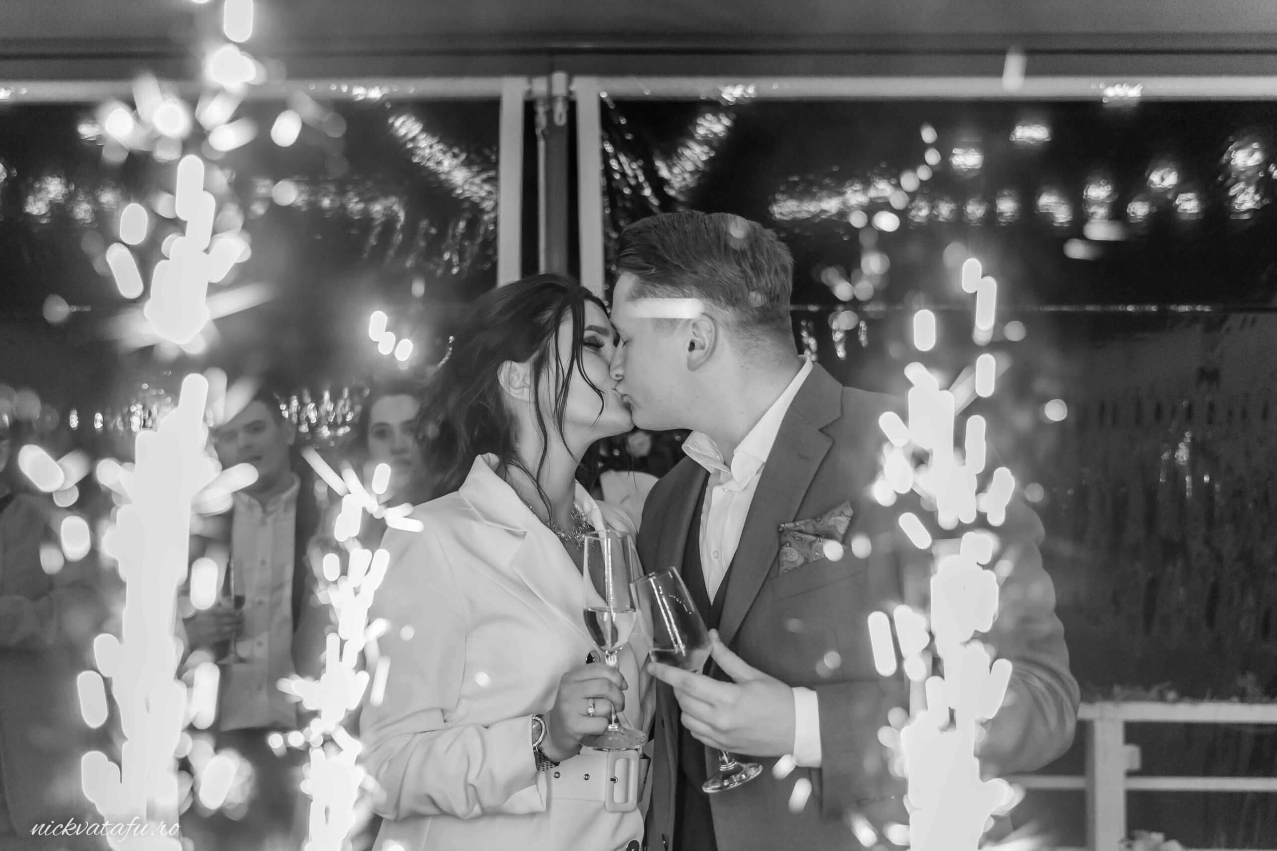 Mire și mireasă sărutându-se în mijlocul artificiilor, fotografie de nuntă plină de emoție și magie.